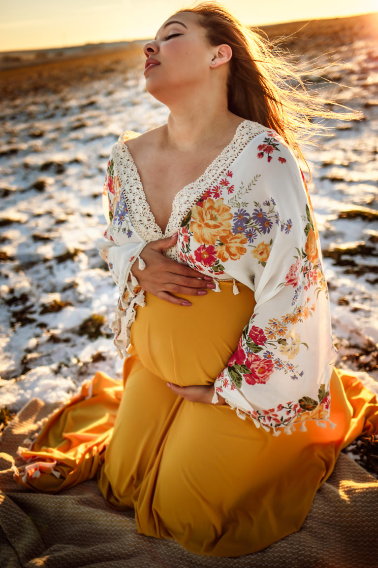 Maternity session with mother kneeling hugging her belly while soaking in the sunlight.